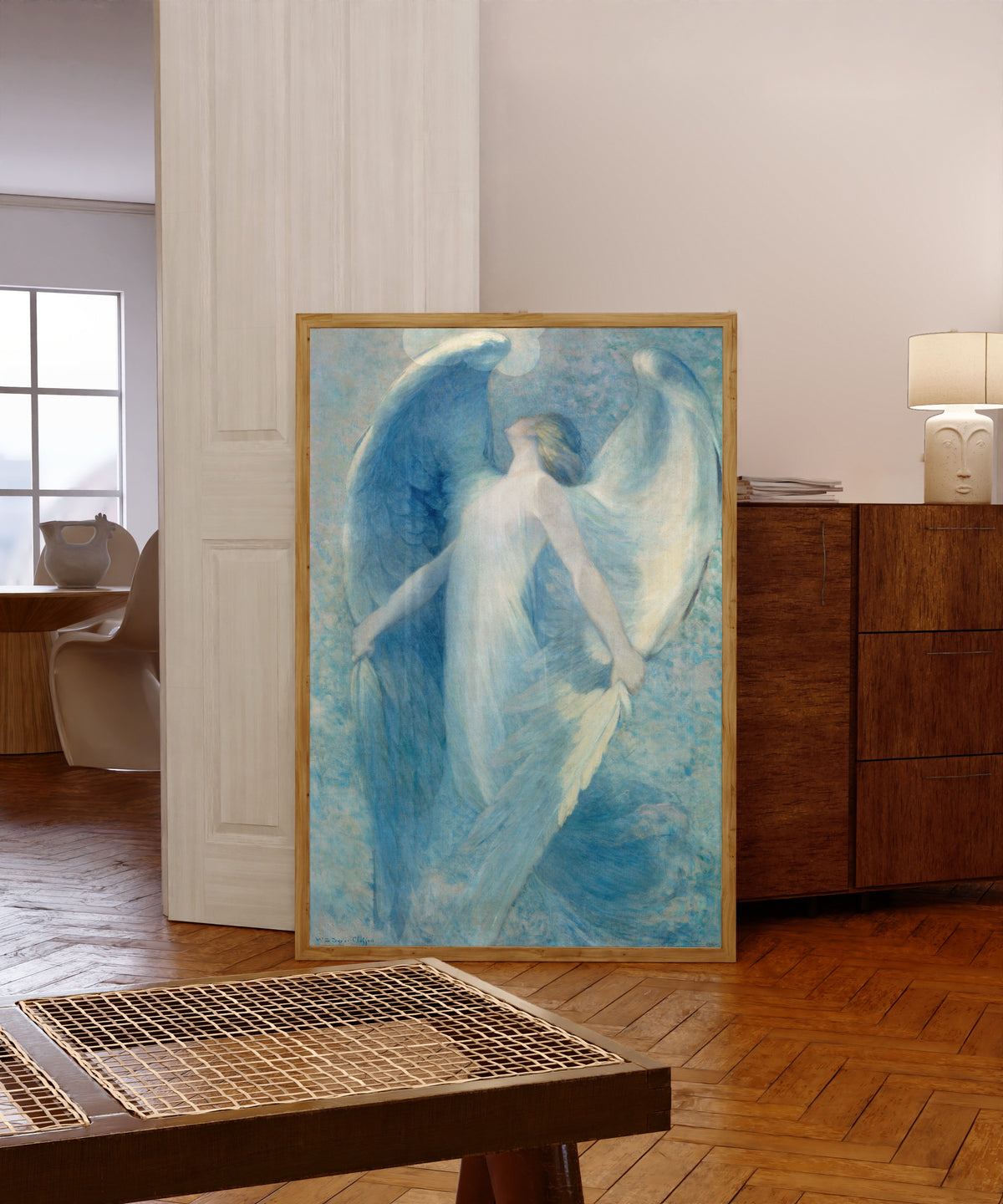 Framed art print of The Angel by William Baxter Closson, in a light wood frame leaning in a warm room with a parquet floor