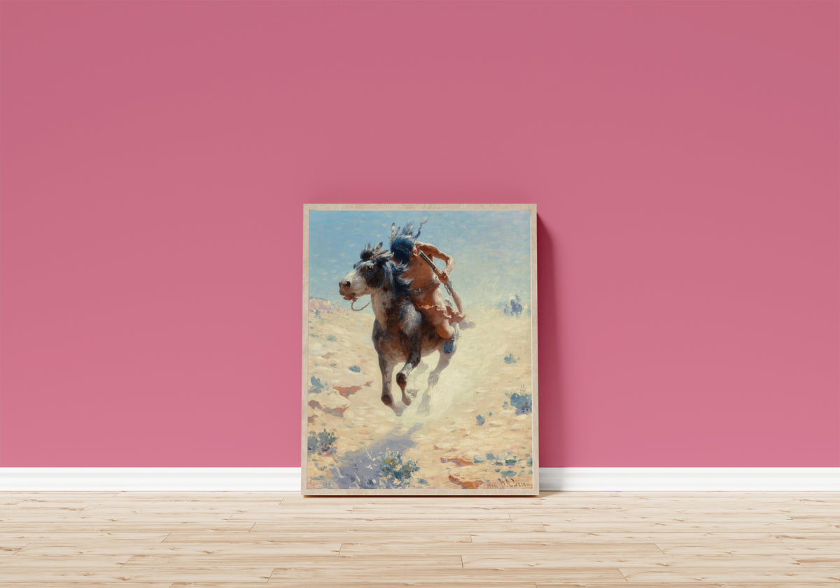 Framed art print of Indian Rider by William Robinson Leigh, in a light wood frame leaning on a pink wall above a wooden floor