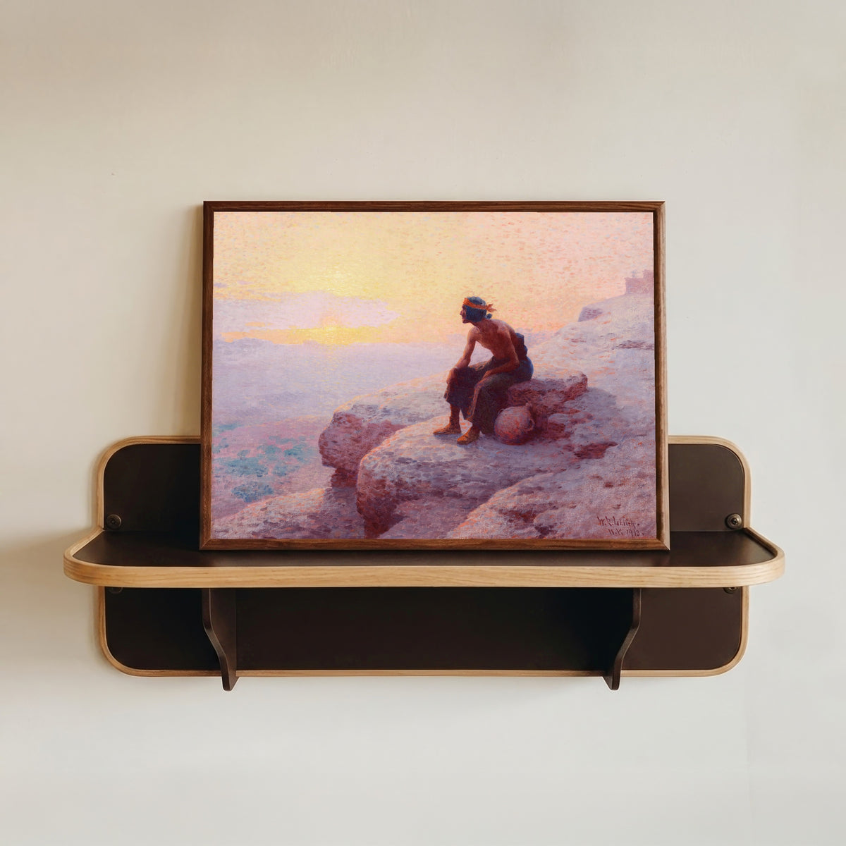 Framed art print of The Water Carrier by William Robinson Leigh, in a dark wood frame resting on a wall shelf