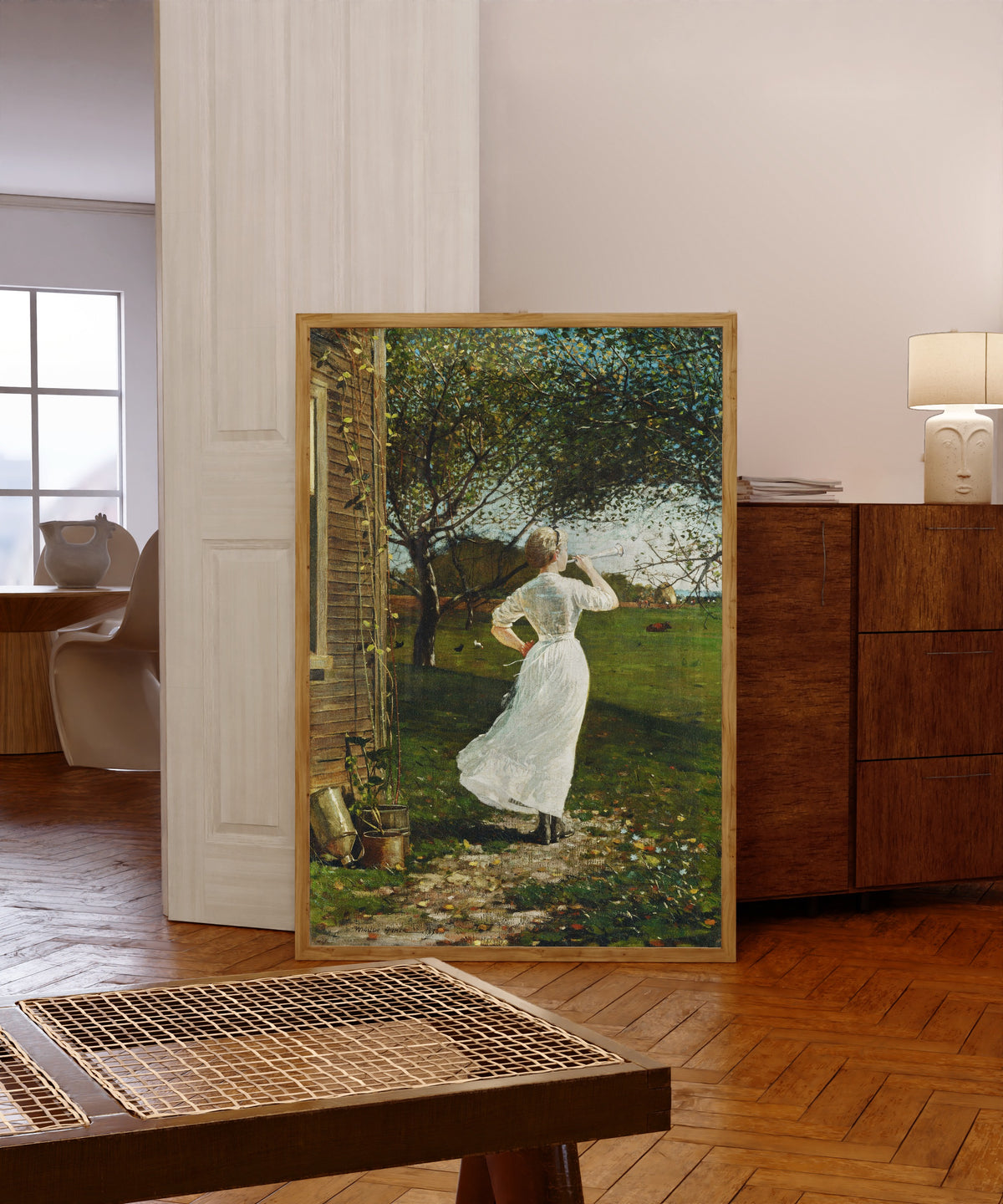 Framed art print of The Dinner Horn by Winslow Homer, in a light wood frame leaning in a warm room with a parquet floor