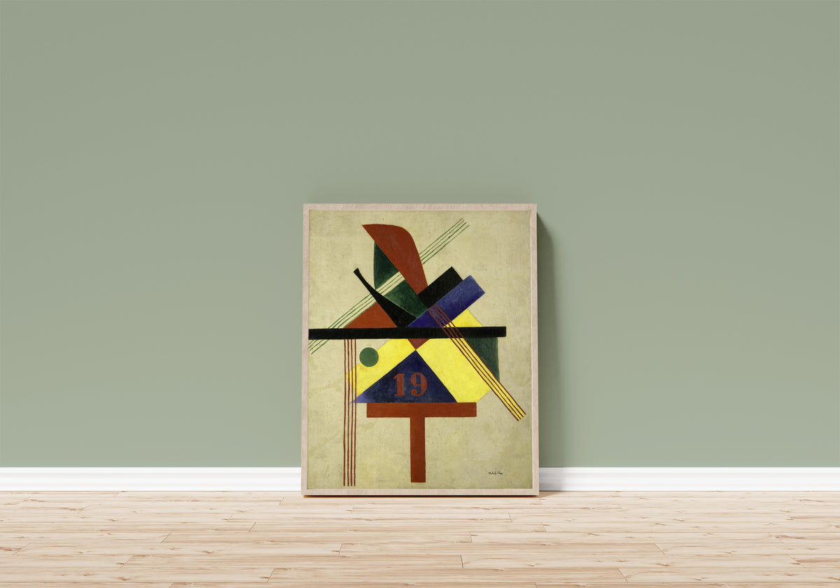 Framed art print of 19 by László Moholy-Nagy, in a light wood frame leaning on a sage green wall above a wooden floor