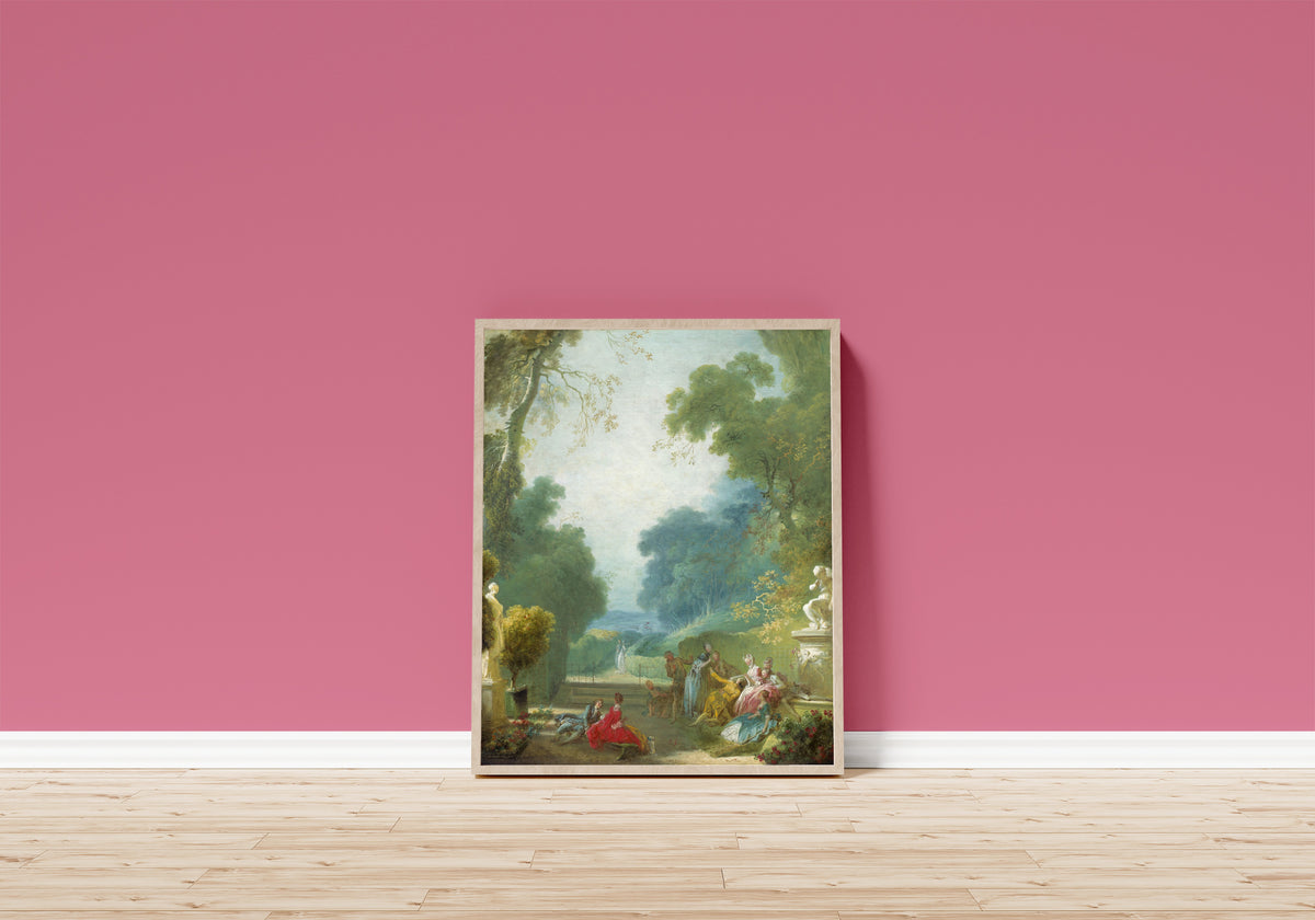 Framed art print of A Game of Hot Cockles by Jean-Honoré Fragonard, in a light wood frame leaning on a pink wall above a wooden floor