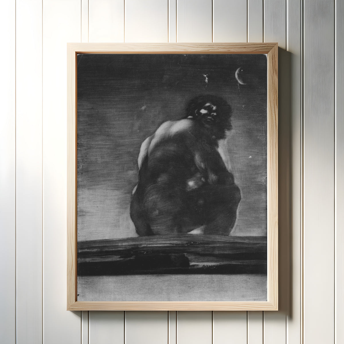 Framed art print of A Giant Seated in a Landscape (The Colossus) by Francisco de Goya, in a light wood frame on a white panelled wall