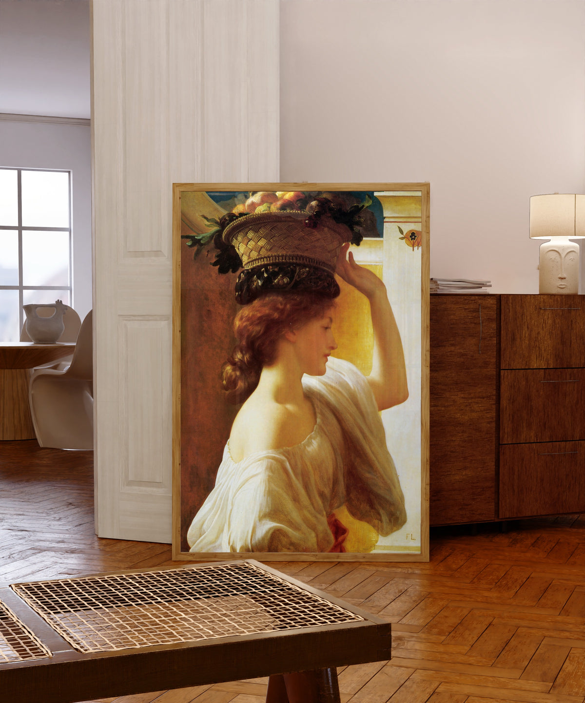 Framed art print of A Girl with a Basket of Fruit by Frederic Leighton, in a light wood frame leaning in a warm room with a parquet floor