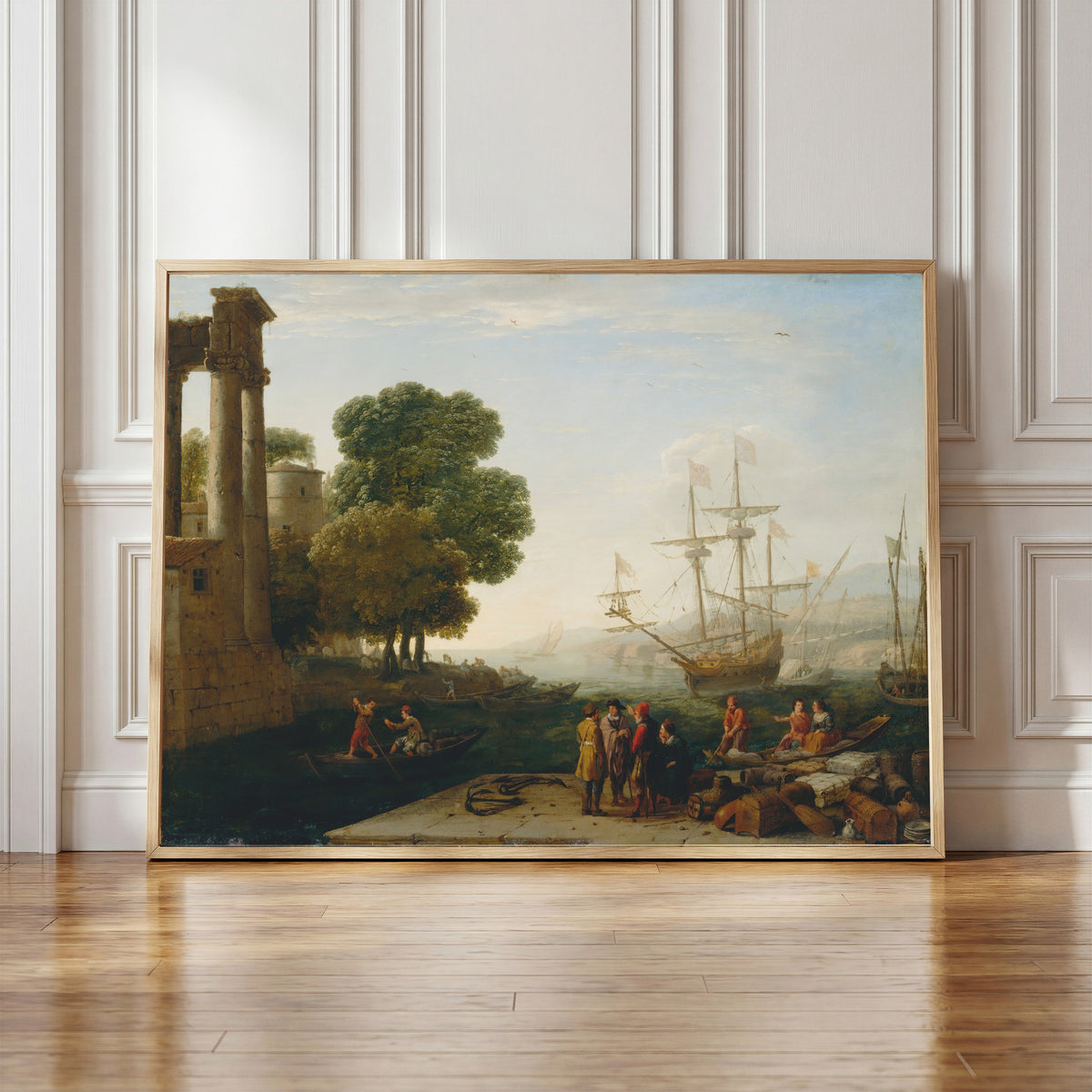 Framed art print of A Seaport at Sunset by Claude Lorrain, in a light wood frame leaning against a panelled white wall