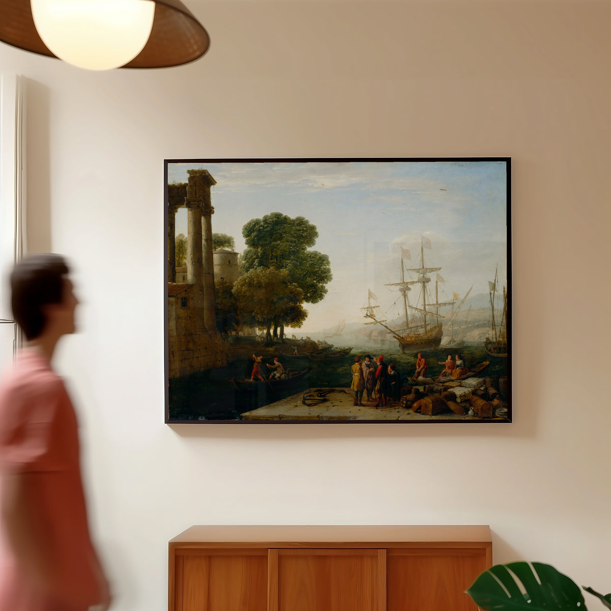 Framed art print of A Seaport at Sunset by Claude Lorrain, in a slim black frame on a warm wall in a sunlit room