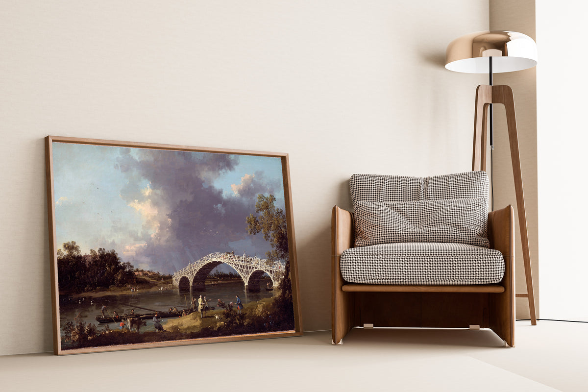 Framed art print of A View of Walton Bridge by Canaletto, leaning against a wall beside an armchair and a floor lamp