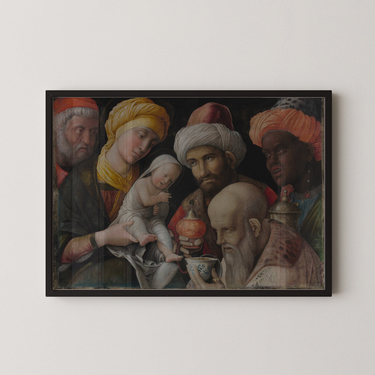 Framed art print of Adoration of the Magi by Andrea Mantegna, in a black frame on a pale wall