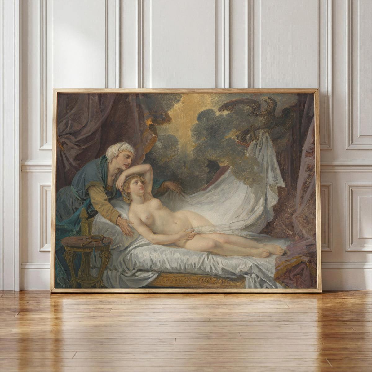 Framed art print of Aegina Visited by Jupiter by Jean-Baptiste Greuze, in a light wood frame leaning against a panelled white wall