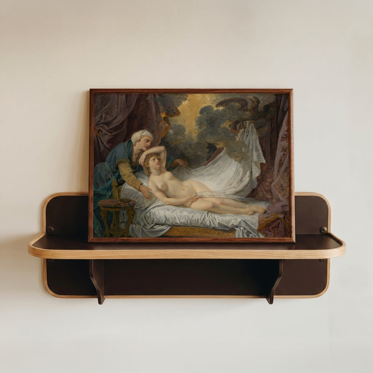 Framed art print of Aegina Visited by Jupiter by Jean-Baptiste Greuze, in a dark wood frame resting on a wall shelf