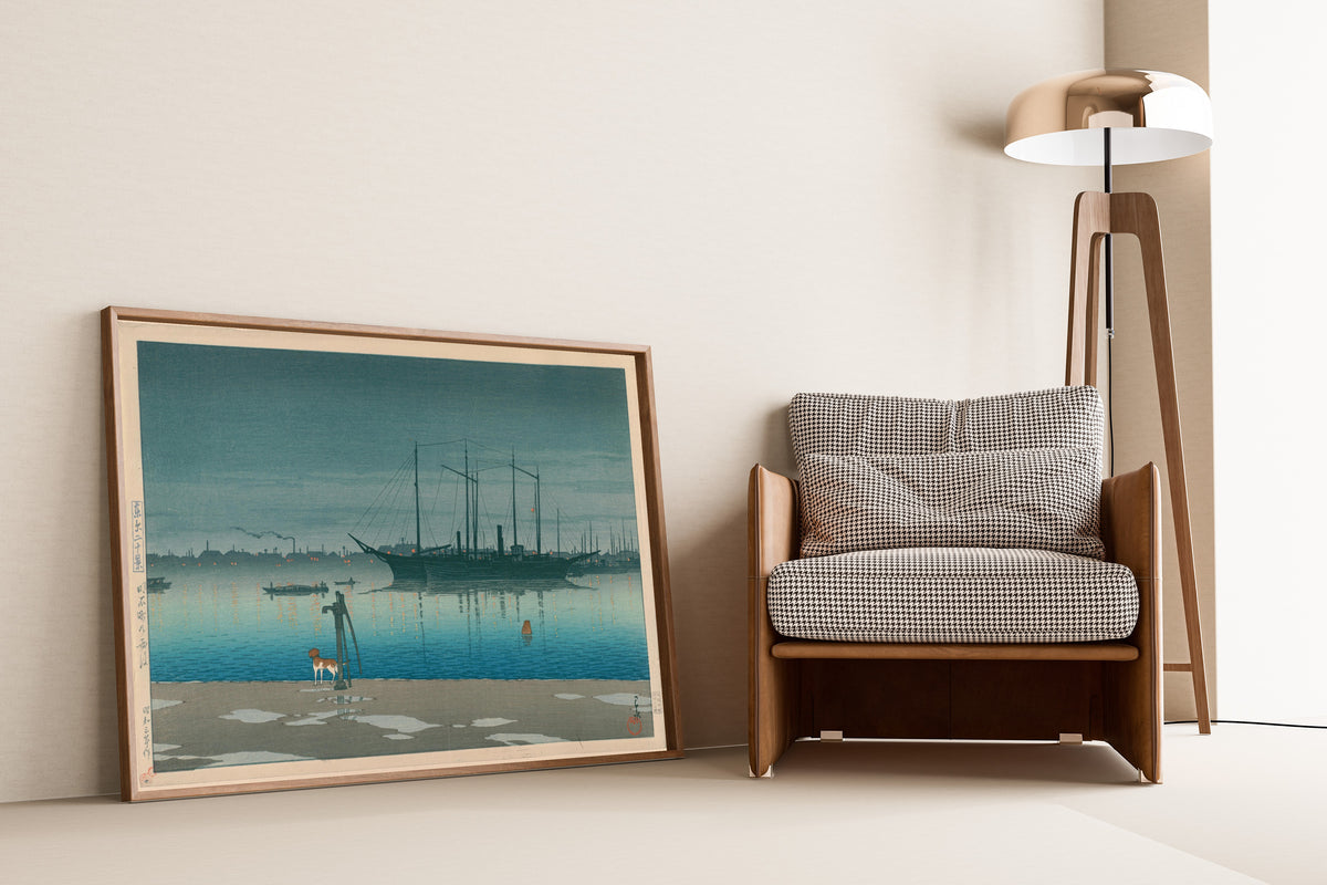 Framed art print of Akashi-cho After Rain by Kawase Hasui, leaning against a wall beside an armchair and a floor lamp