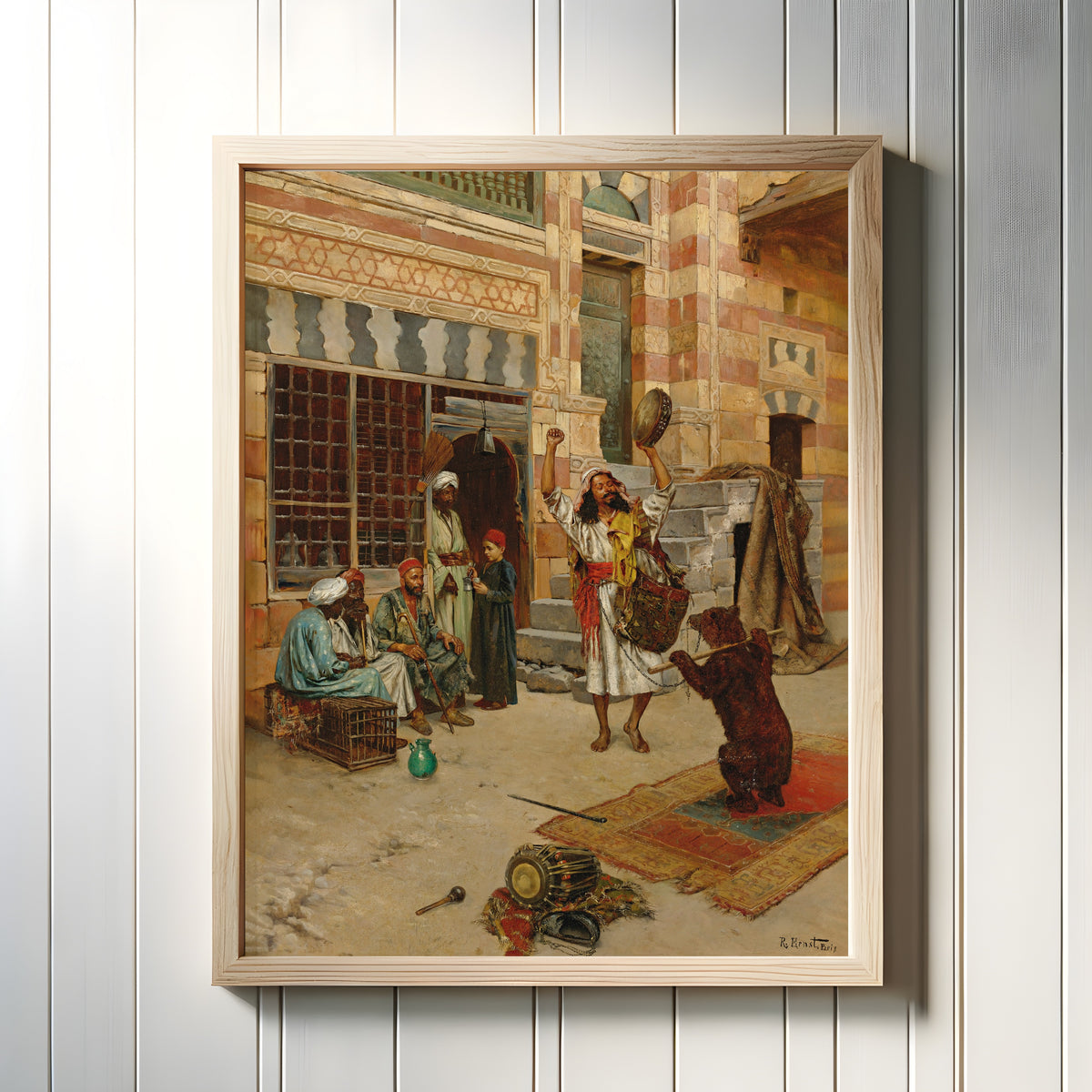 Framed art print of An Afternoon Show by Rudolf Ernst, in a light wood frame on a white panelled wall