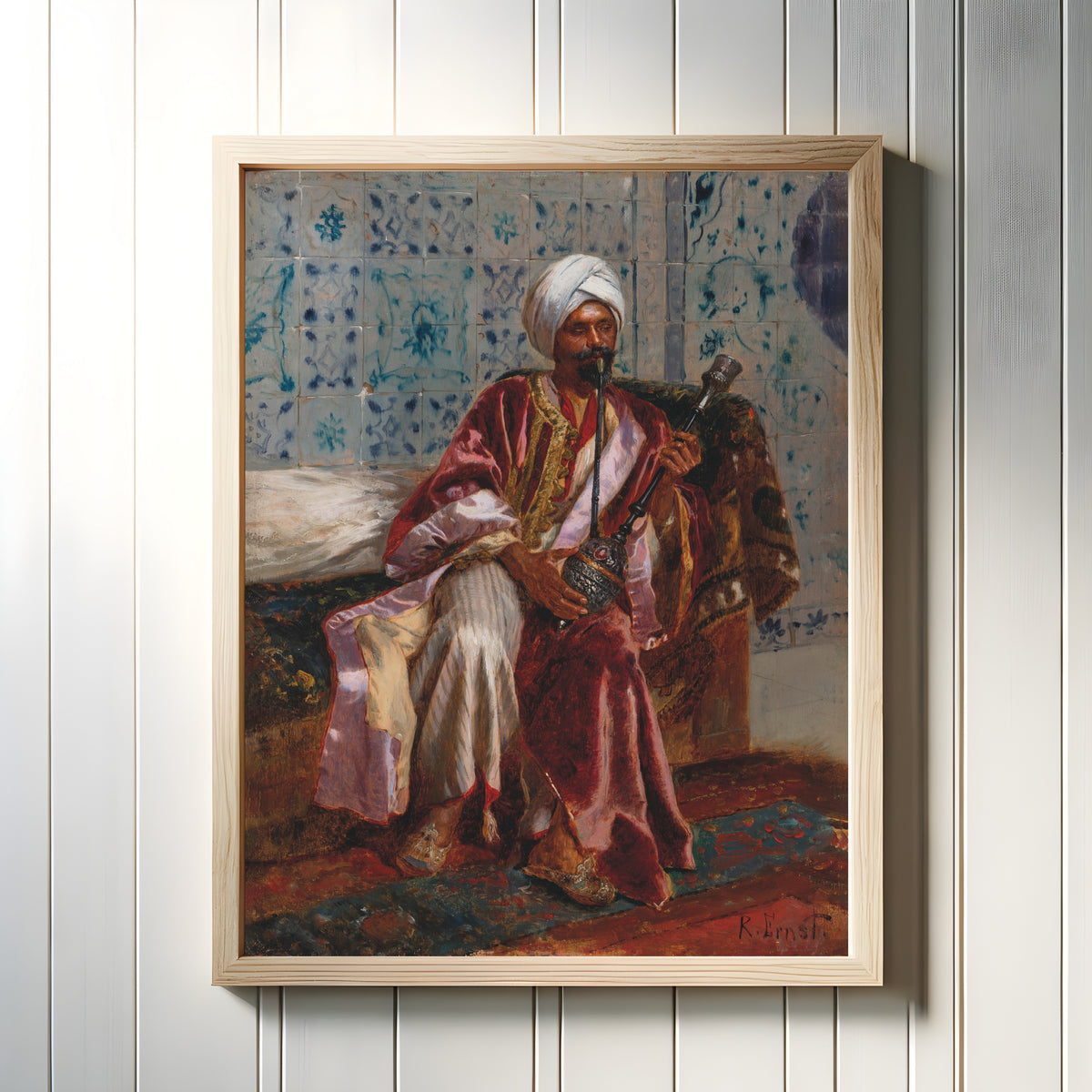 Framed art print of Arab smoking a nargilah by Rudolf Ernst, in a light wood frame on a white panelled wall