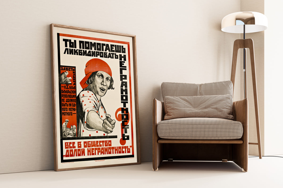 Framed art print of Are You Helping to Eliminate Illiteracy?, leaning against a wall beside an armchair and a floor lamp