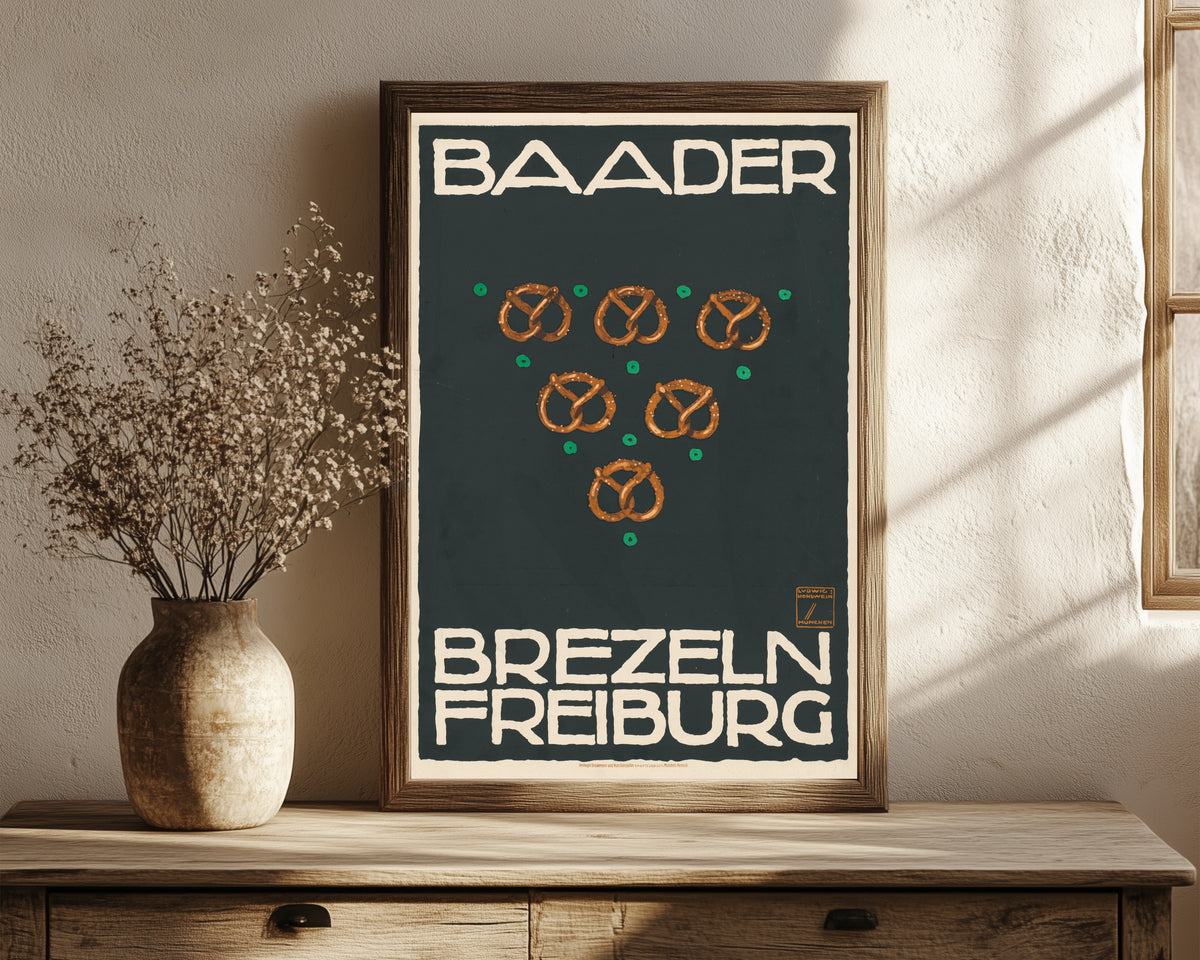 Framed art print of Baader Brezeln, Freiburg by Ludwig Hohlwein, in a dark wood frame leaning on a rustic console beside dried flowers