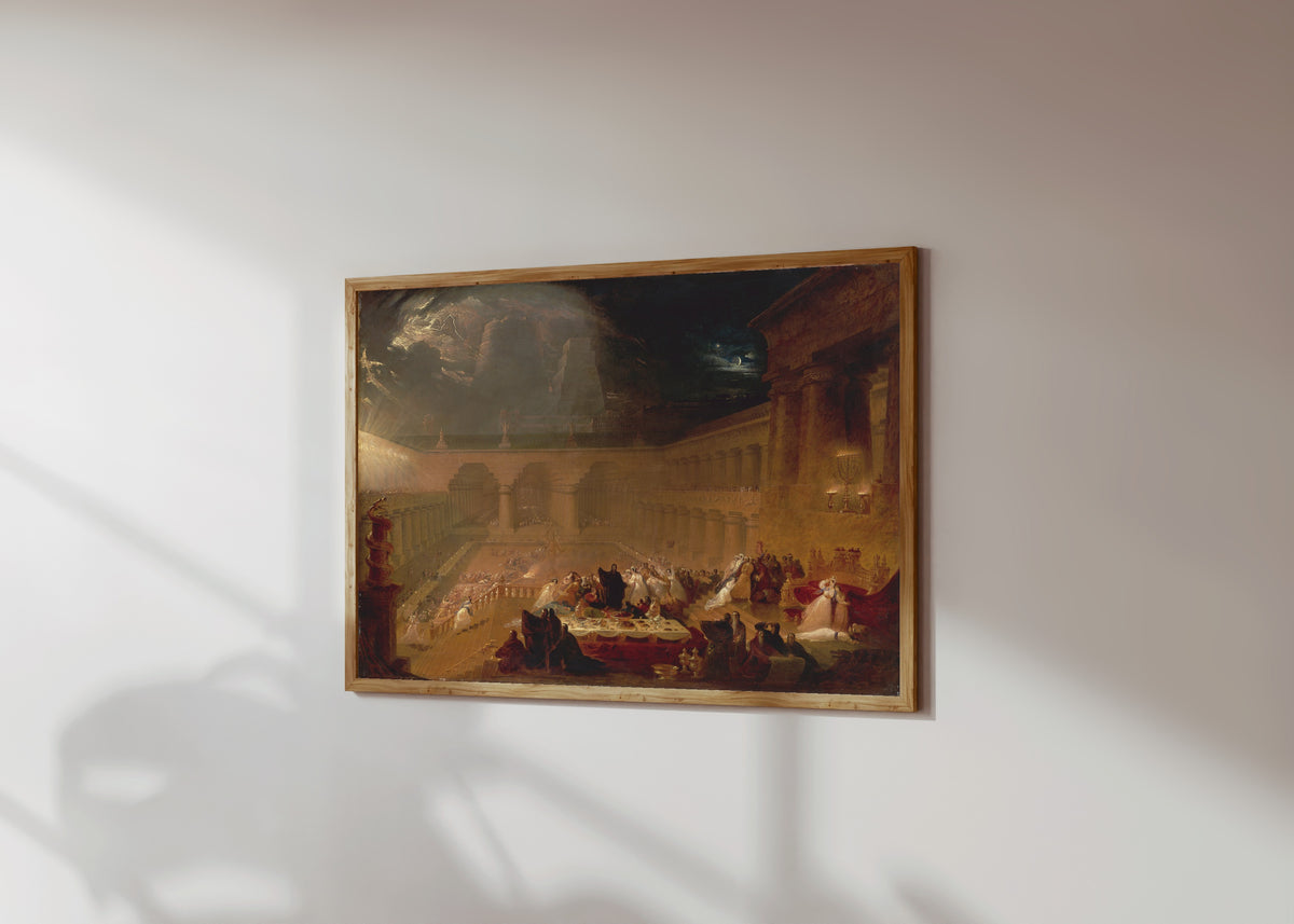 Framed art print of Belshazzar's Feast by John Martin, in a light wood frame on a sunlit white wall, seen at a slight angle