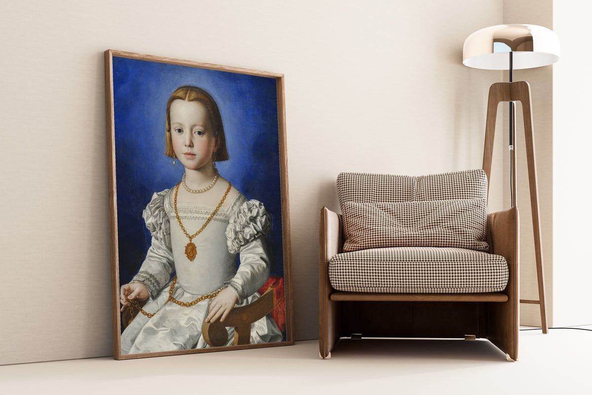 Framed art print of Bia di Cosimo de’ Medici by Bronzino, leaning against a wall beside an armchair and a floor lamp