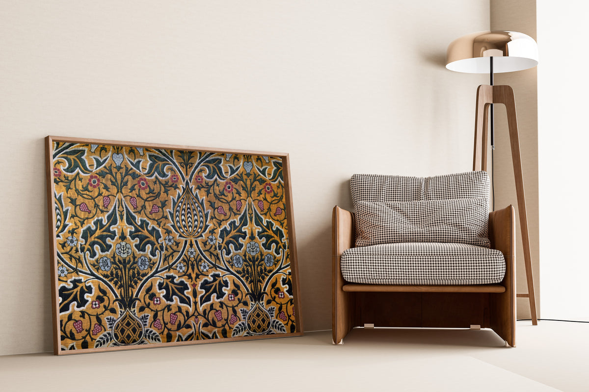 Framed art print of Brocatel by William Morris, leaning against a wall beside an armchair and a floor lamp