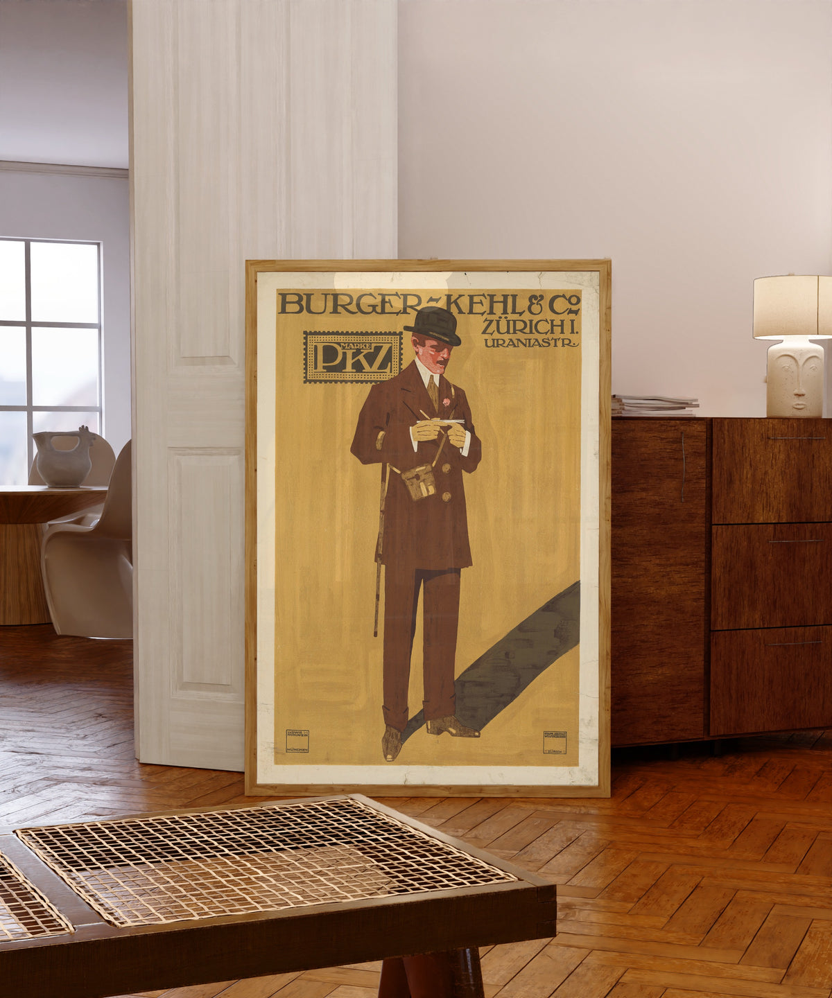 Framed art print of Burger-Kehl & Co, Zürich: Marke PKZ by Ludwig Hohlwein, in a light wood frame leaning in a warm room with a parquet floor