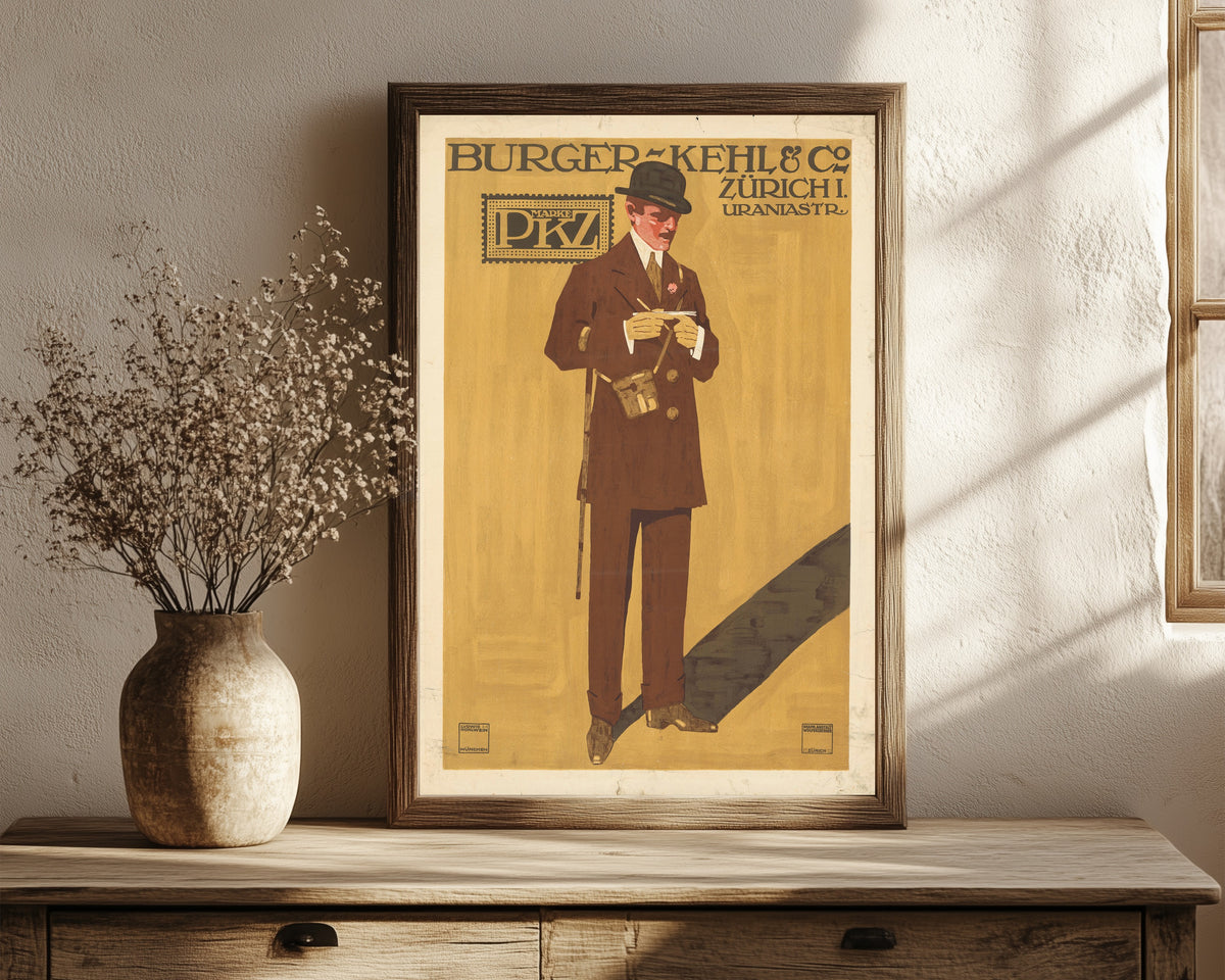 Framed art print of Burger-Kehl & Co, Zürich: Marke PKZ by Ludwig Hohlwein, in a dark wood frame leaning on a rustic console beside dried flowers