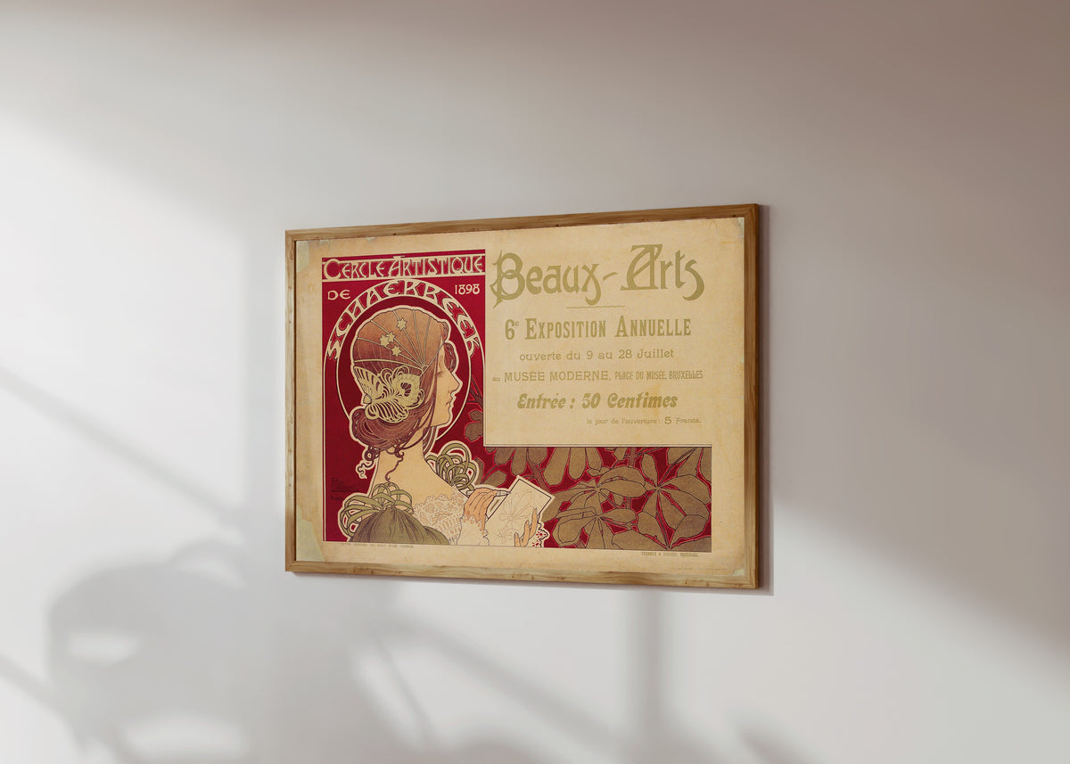 Framed art print of Cercle Artistique de Schaerbeek (1898) by Henri Privat-Livemont, in a light wood frame on a sunlit white wall, seen at a slight angle