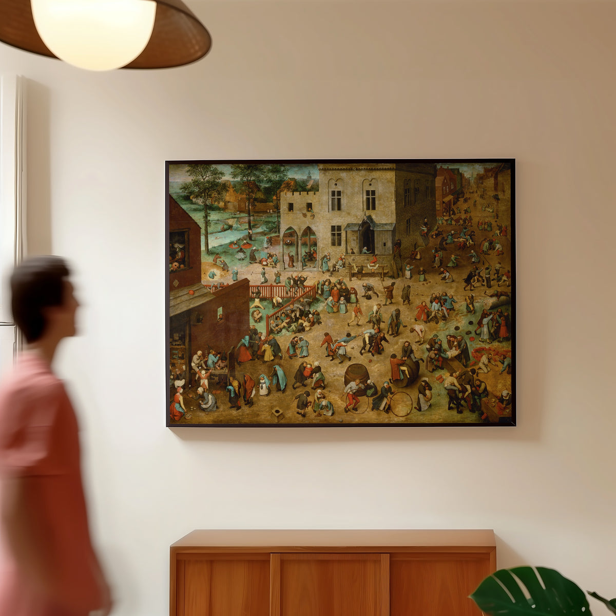 Framed art print of Children's Games by Pieter Bruegel the Elder, in a slim black frame on a warm wall in a sunlit room