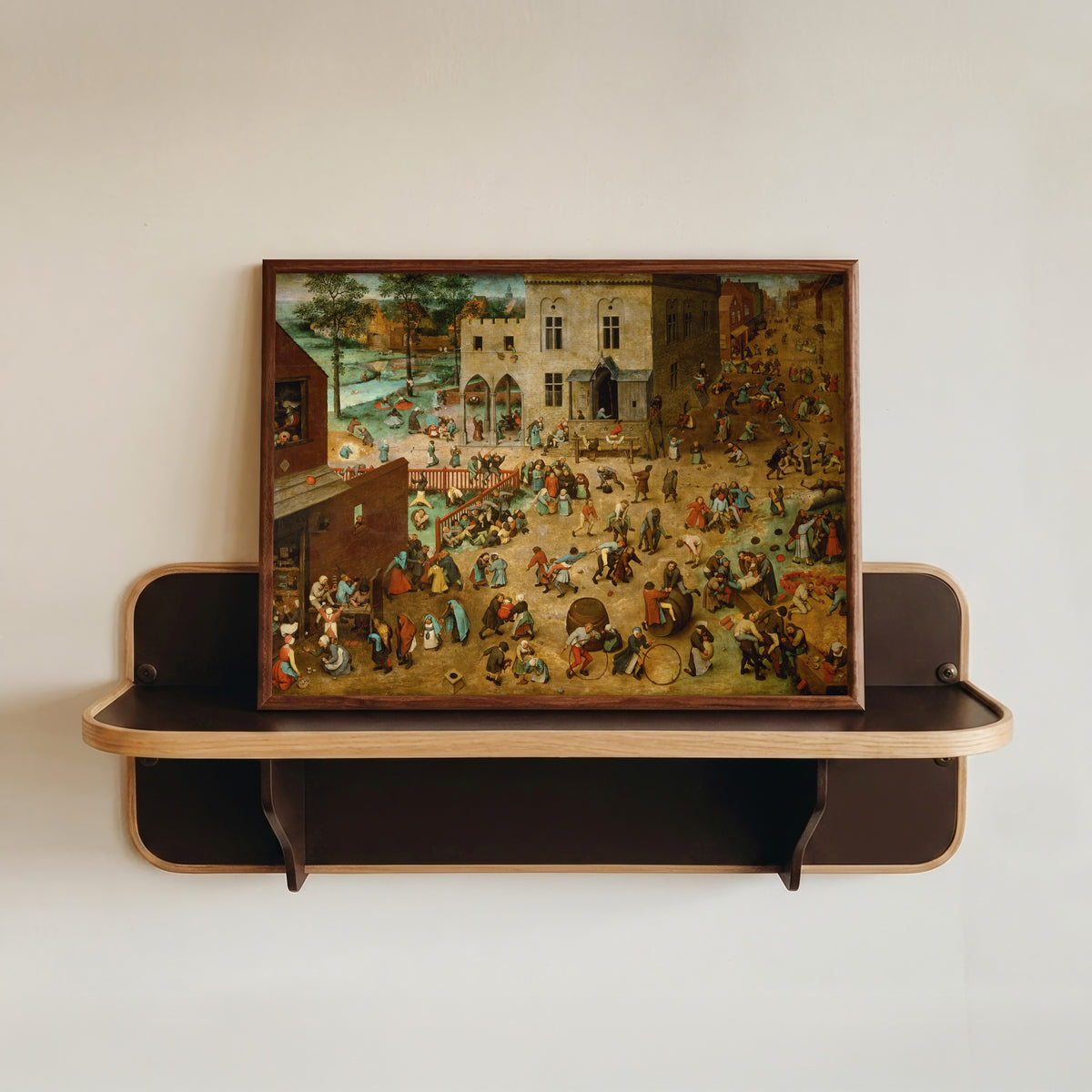 Framed art print of Children's Games by Pieter Bruegel the Elder, in a dark wood frame resting on a wall shelf