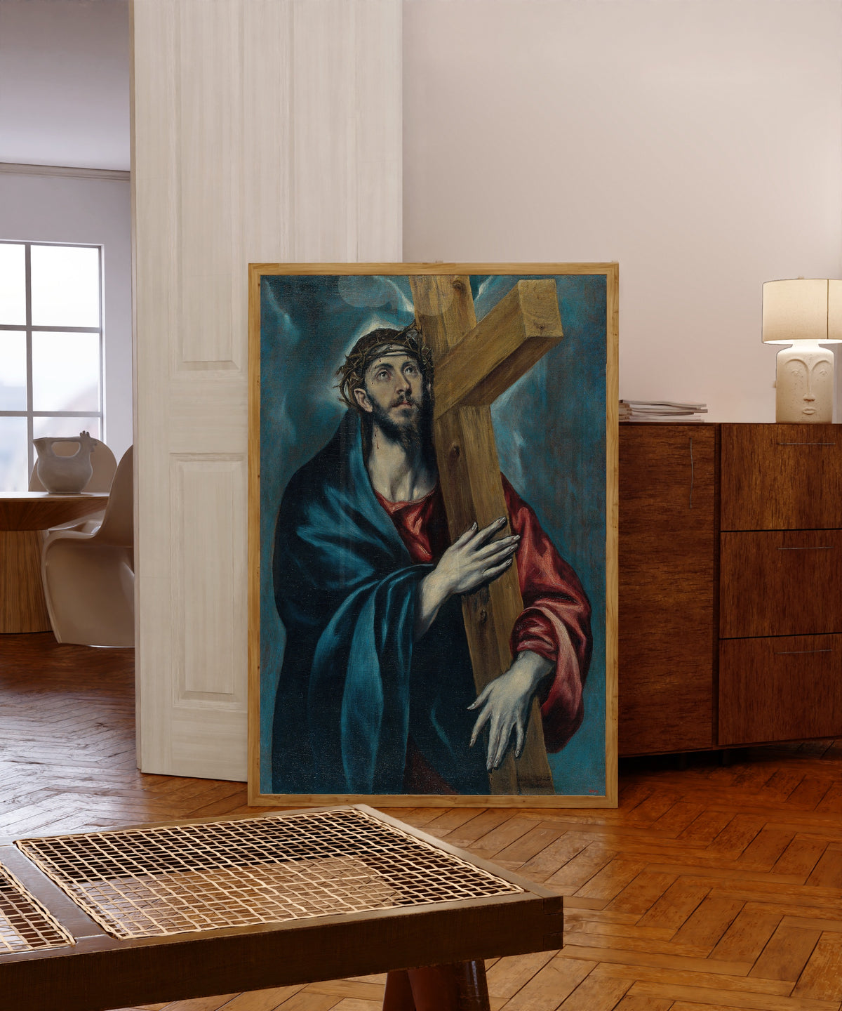 Framed art print of Christ with the Cross by El Greco, in a light wood frame leaning in a warm room with a parquet floor