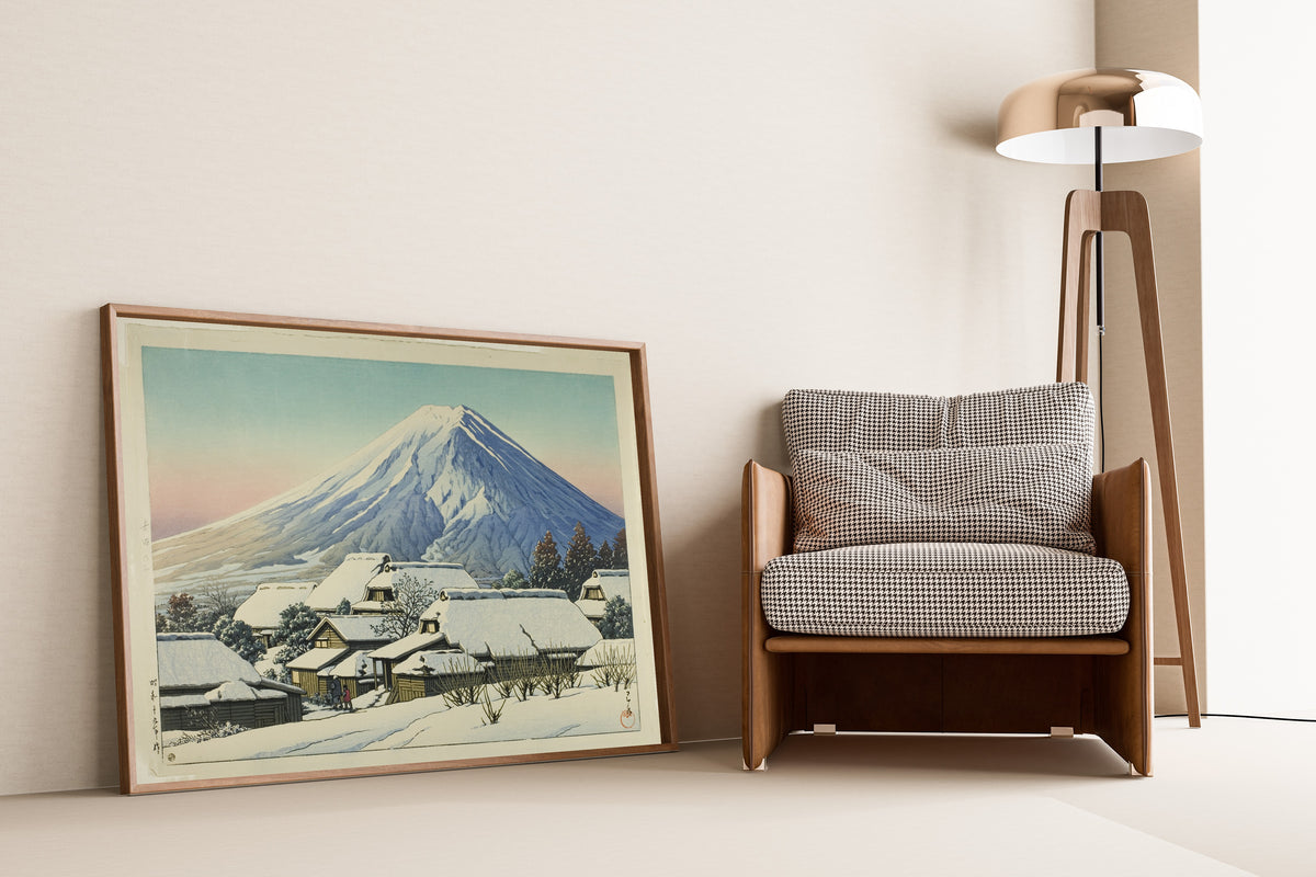 Framed art print of Clearing after a Snowfall, Yoshida by Kawase Hasui, leaning against a wall beside an armchair and a floor lamp