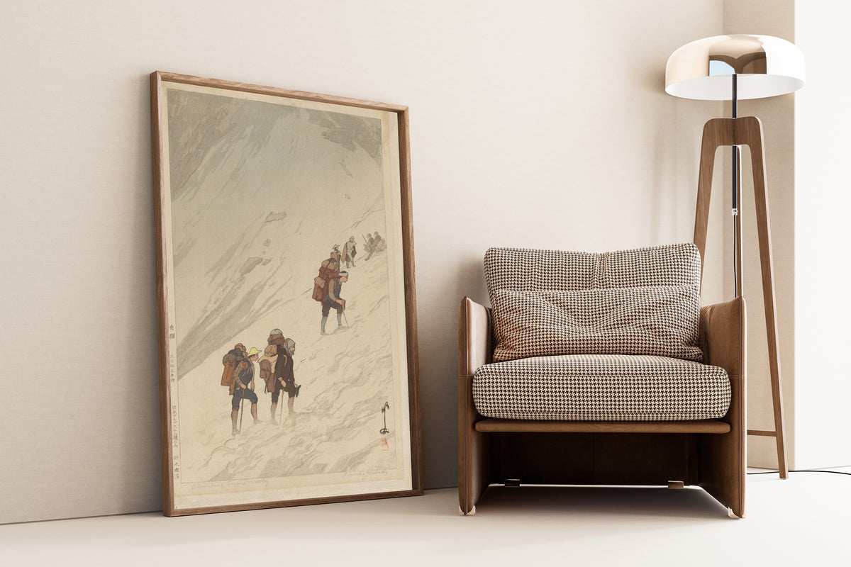 Framed art print of Climbing a Snow Valley at Harinoki by Hiroshi Yoshida, leaning against a wall beside an armchair and a floor lamp
