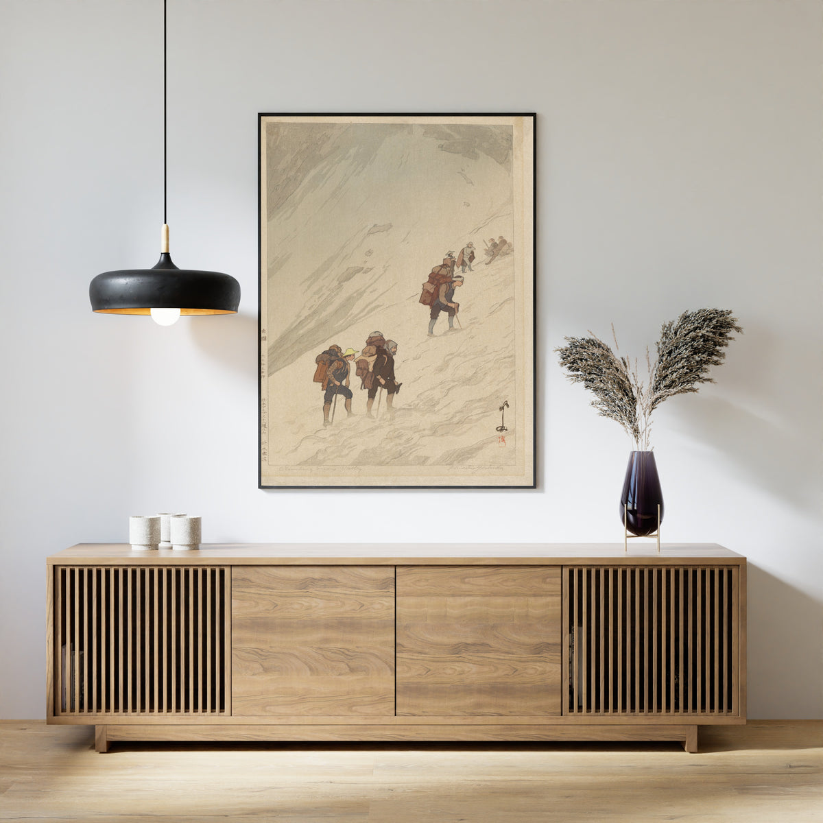 Framed art print of Climbing a Snow Valley at Harinoki by Hiroshi Yoshida, above a slatted wood sideboard