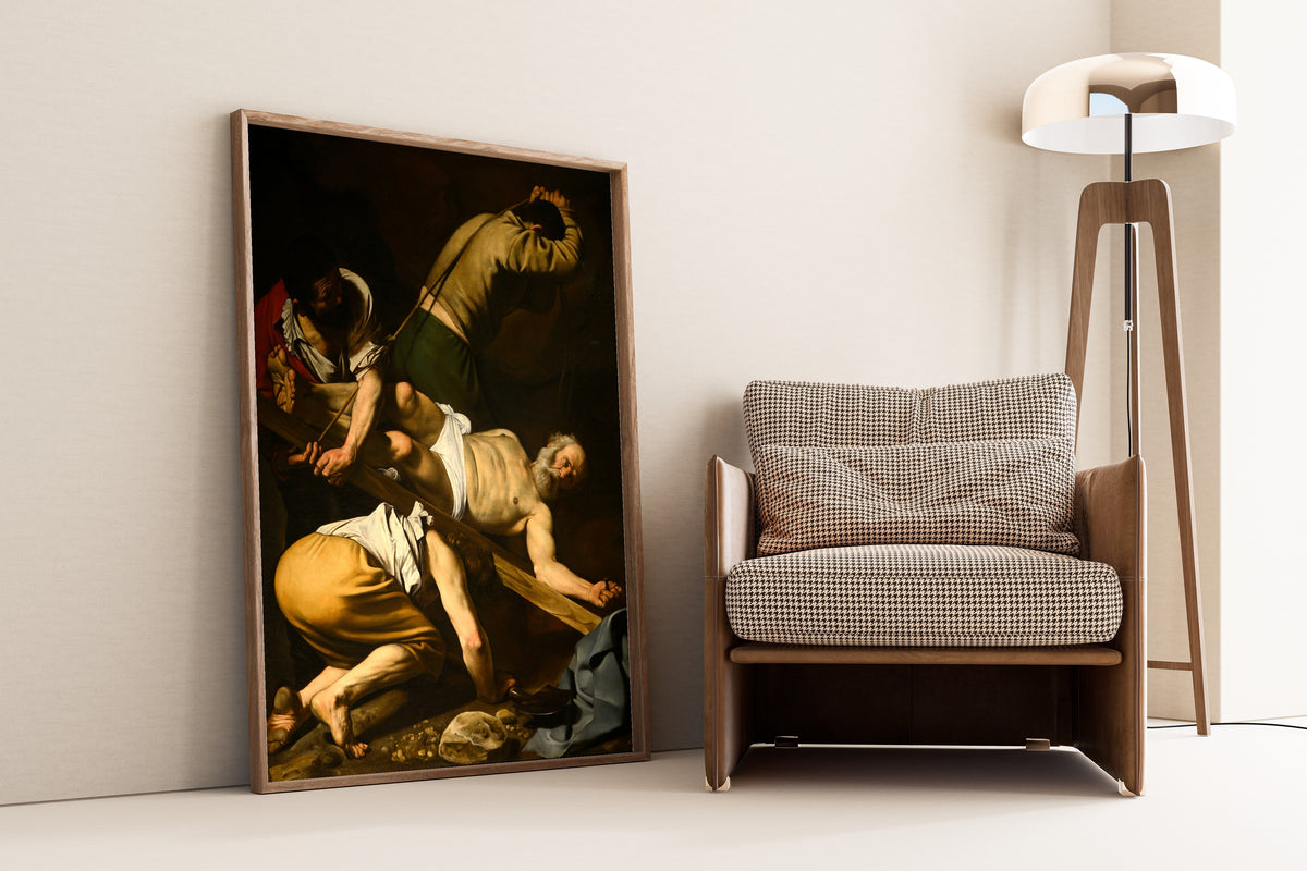 Framed art print of Crucifixion of St. Peter by Caravaggio, leaning against a wall beside an armchair and a floor lamp