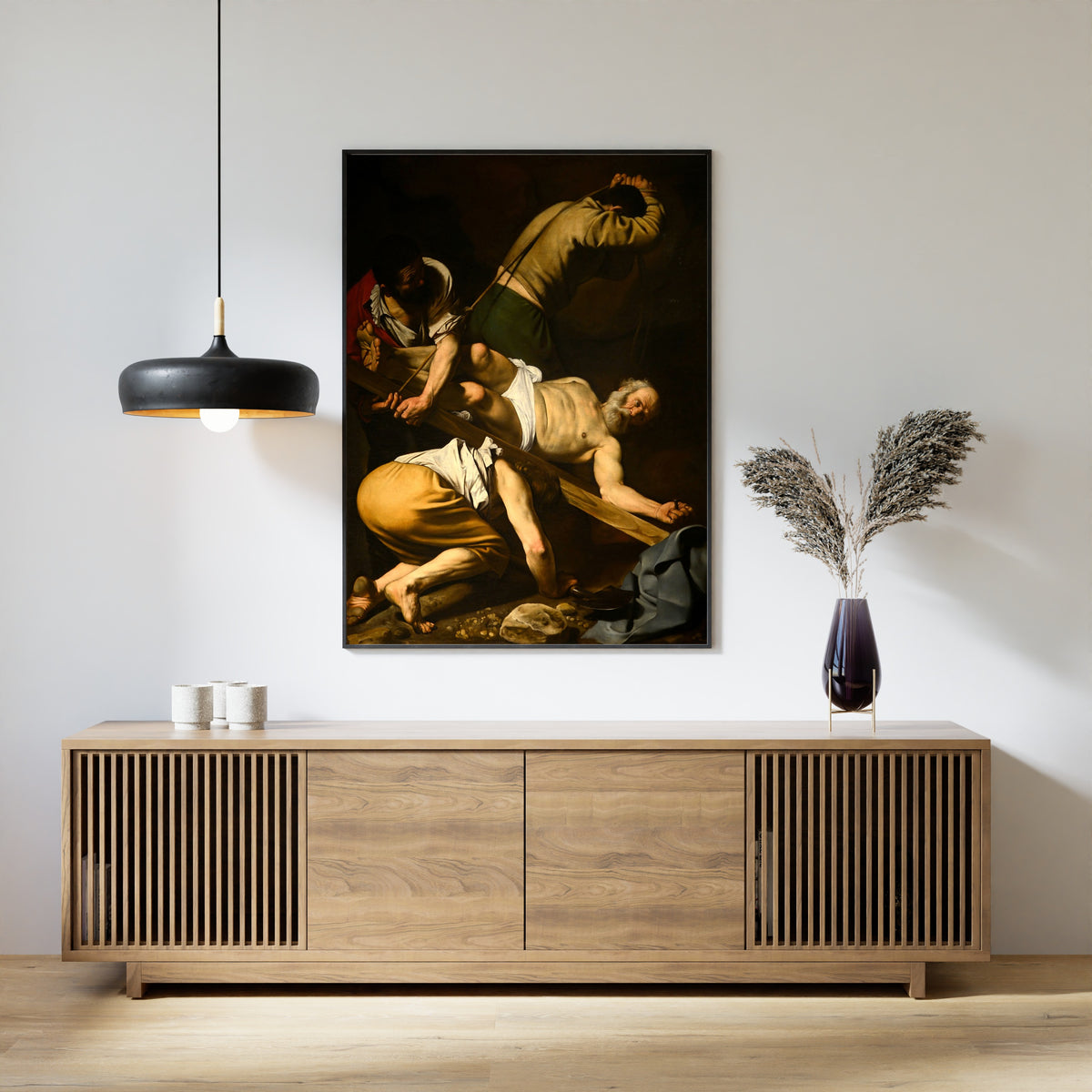 Framed art print of Crucifixion of St. Peter by Caravaggio, above a slatted wood sideboard