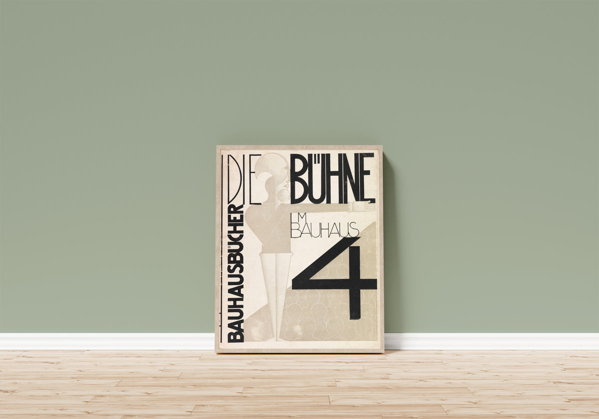 Framed art print of Die Bühne im Bauhaus by Oskar Schlemmer, in a light wood frame leaning on a sage green wall above a wooden floor