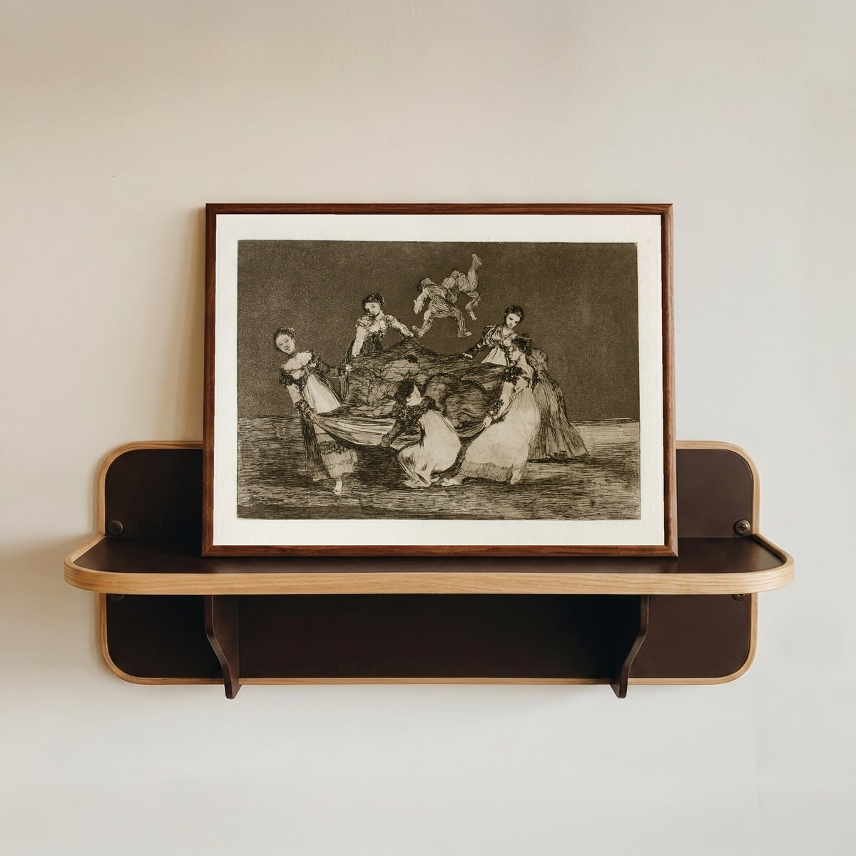 Framed art print of Disparate femenino (Feminine Folly), from Los Disparates by Francisco de Goya, in a dark wood frame resting on a wall shelf