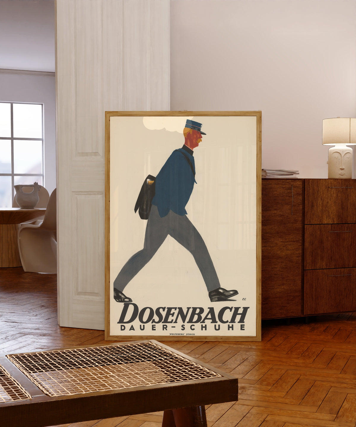 Framed art print of Dosenbach: Dauer-Schuhe by Emil Cardinaux, in a light wood frame leaning in a warm room with a parquet floor