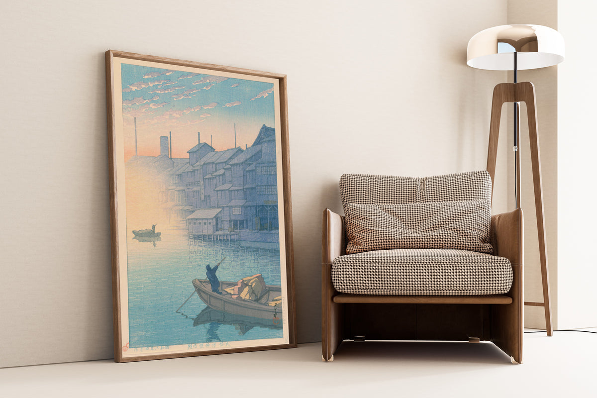 Framed art print of Dotonbori, Osaka, in the Morning (Kansai Series) by Kawase Hasui, leaning against a wall beside an armchair and a floor lamp