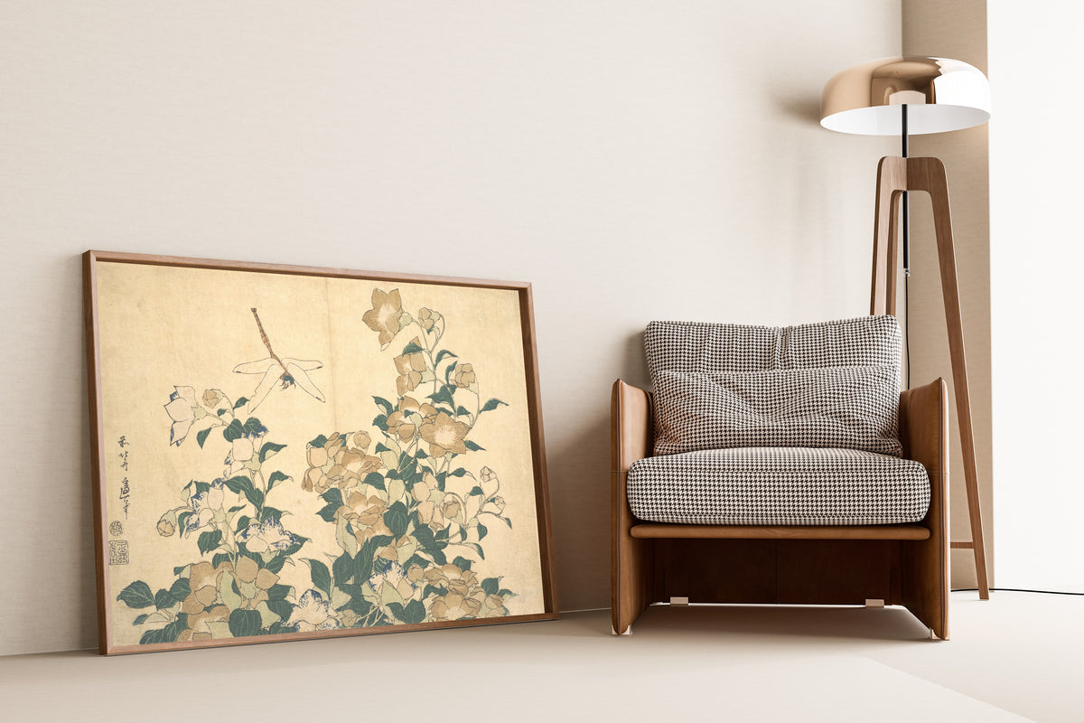 Framed art print of Dragonfly and Bellflower by Katsushika Hokusai, leaning against a wall beside an armchair and a floor lamp