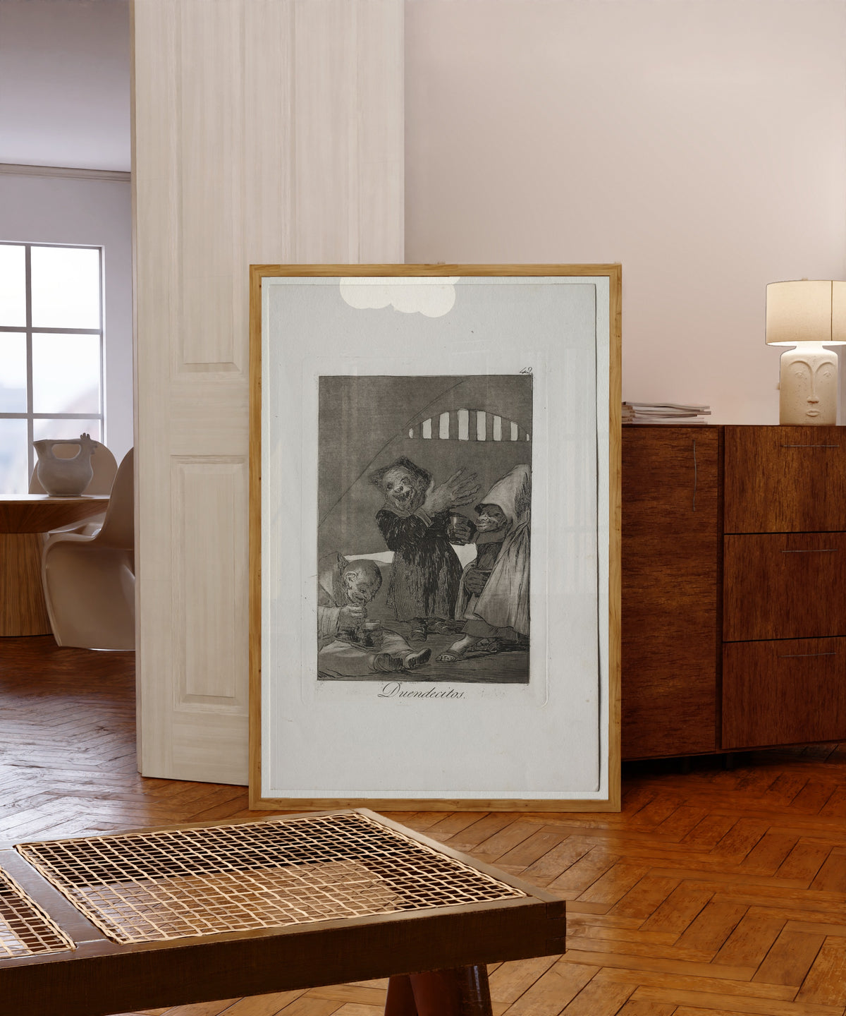 Framed art print of Duendecitos (Hobgoblins), Los Caprichos, Plate 49 by Francisco de Goya, in a light wood frame leaning in a warm room with a parquet floor