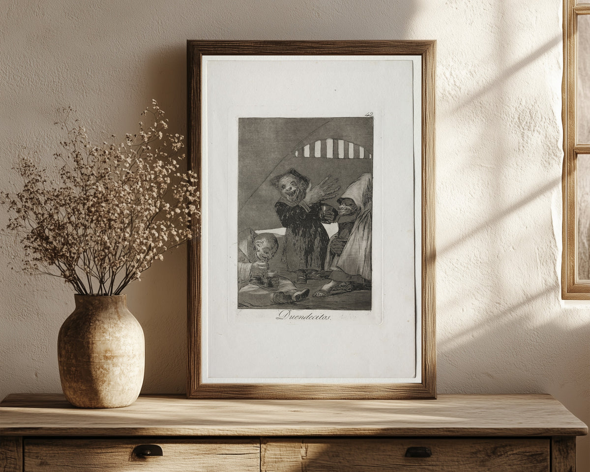 Framed art print of Duendecitos (Hobgoblins), Los Caprichos, Plate… by Francisco de Goya, in a dark wood frame leaning on a rustic console beside dried flowers