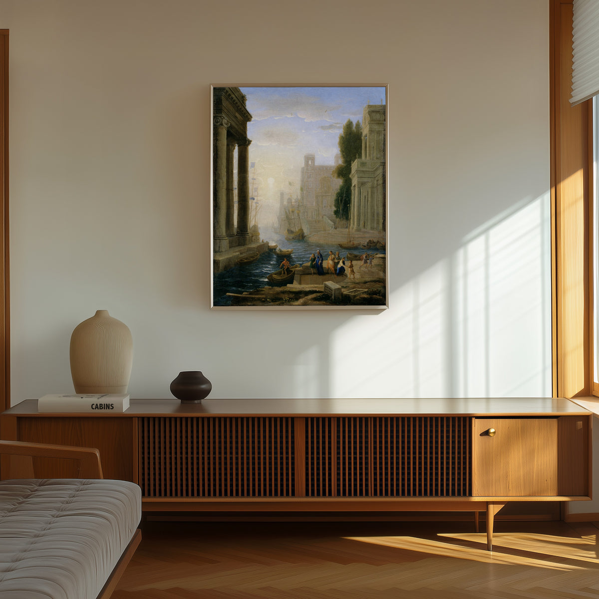 Framed art print of Embarkation of St Paula by Claude Lorrain, in a thin light frame on a sunlit wall above a wooden sideboard