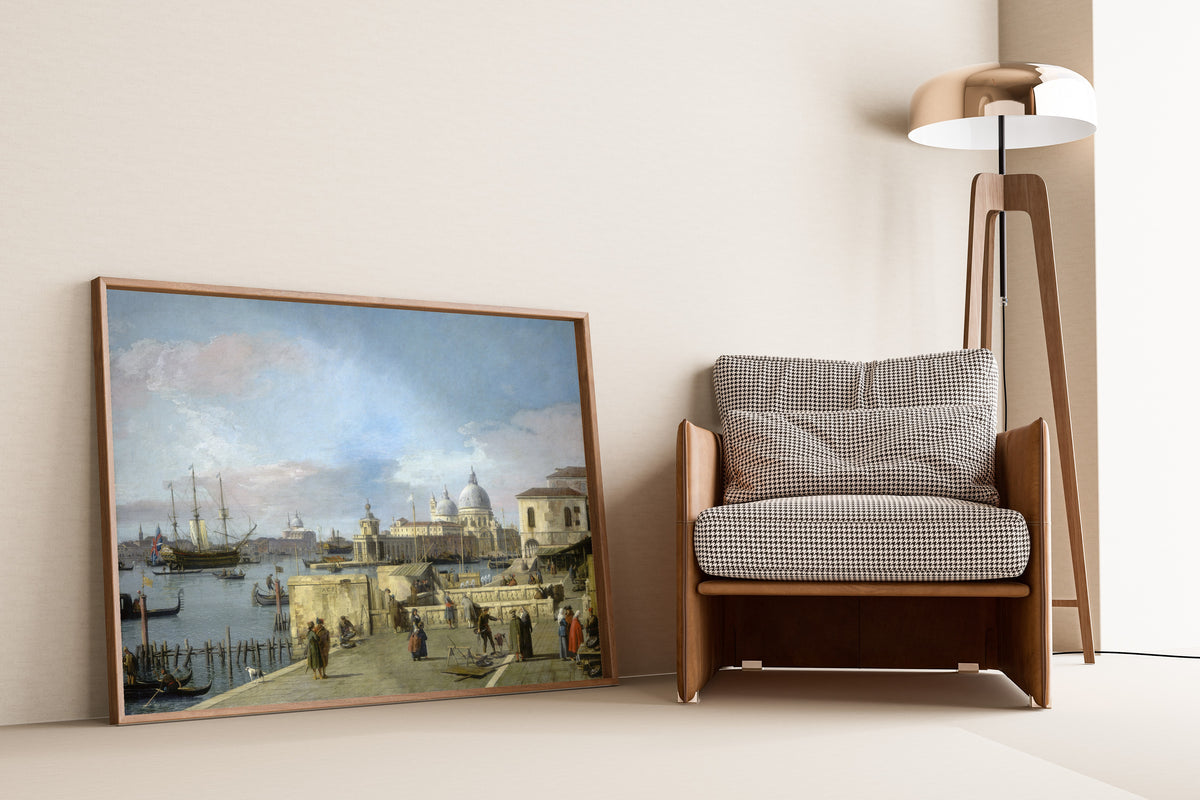 Framed art print of Entrance to the Grand Canal from the Molo, Venice by Canaletto, leaning against a wall beside an armchair and a floor lamp