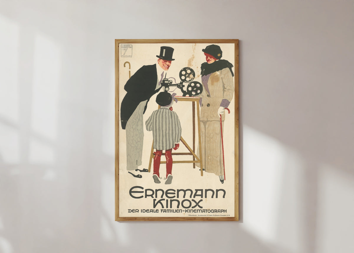 Framed art print of Ernemann Kinox: Der ideale Familien-Kinematograph by Ludwig Hohlwein, in a light wood frame on a sunlit white wall