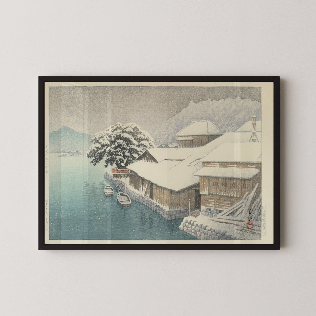 Framed art print of Evening Snow at Ishinomaki by Kawase Hasui, in a black frame on a pale wall