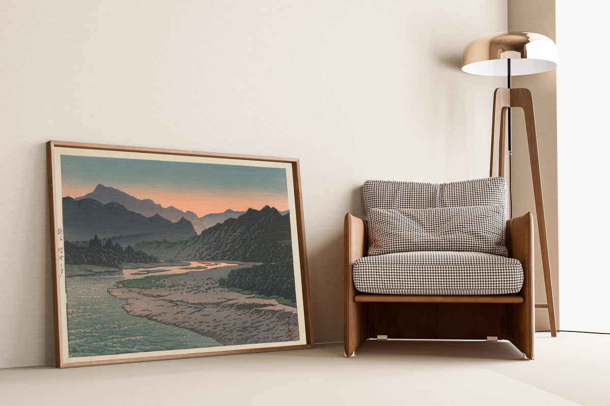 Framed art print of Evening at Minano, Chichibu by Kawase Hasui, leaning against a wall beside an armchair and a floor lamp