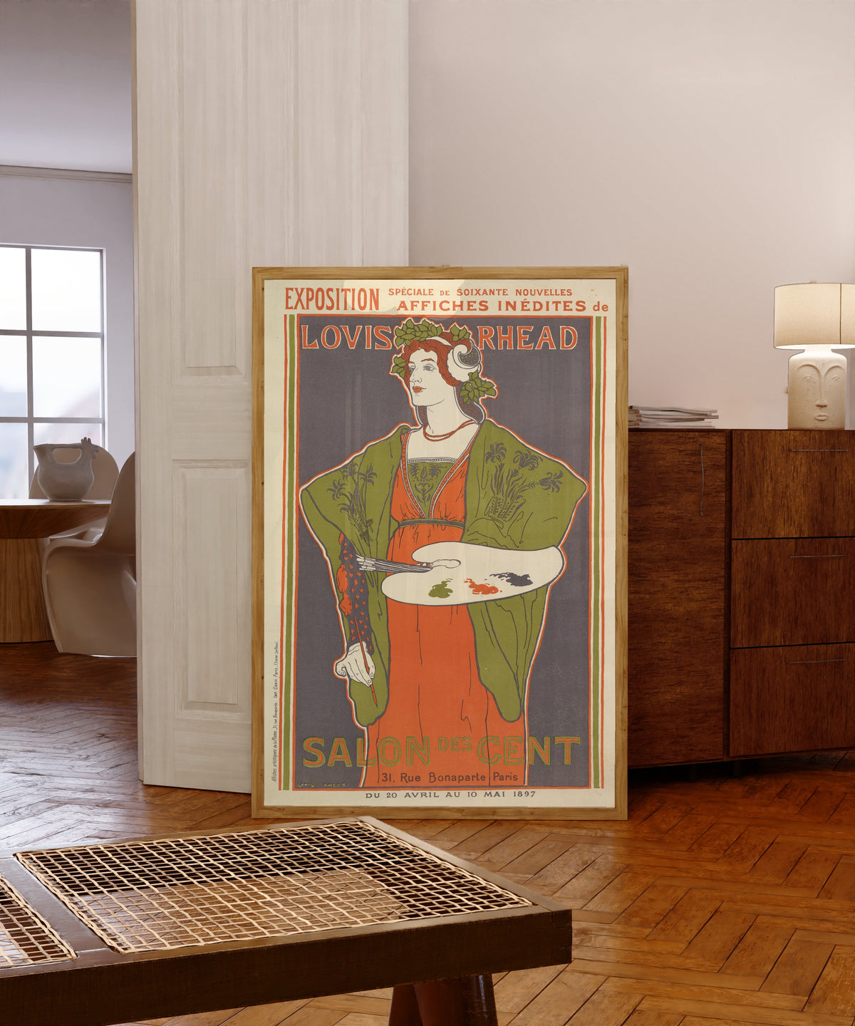 Framed art print of Exposition, Salon des Cent by Louis Rhead, in a light wood frame leaning in a warm room with a parquet floor