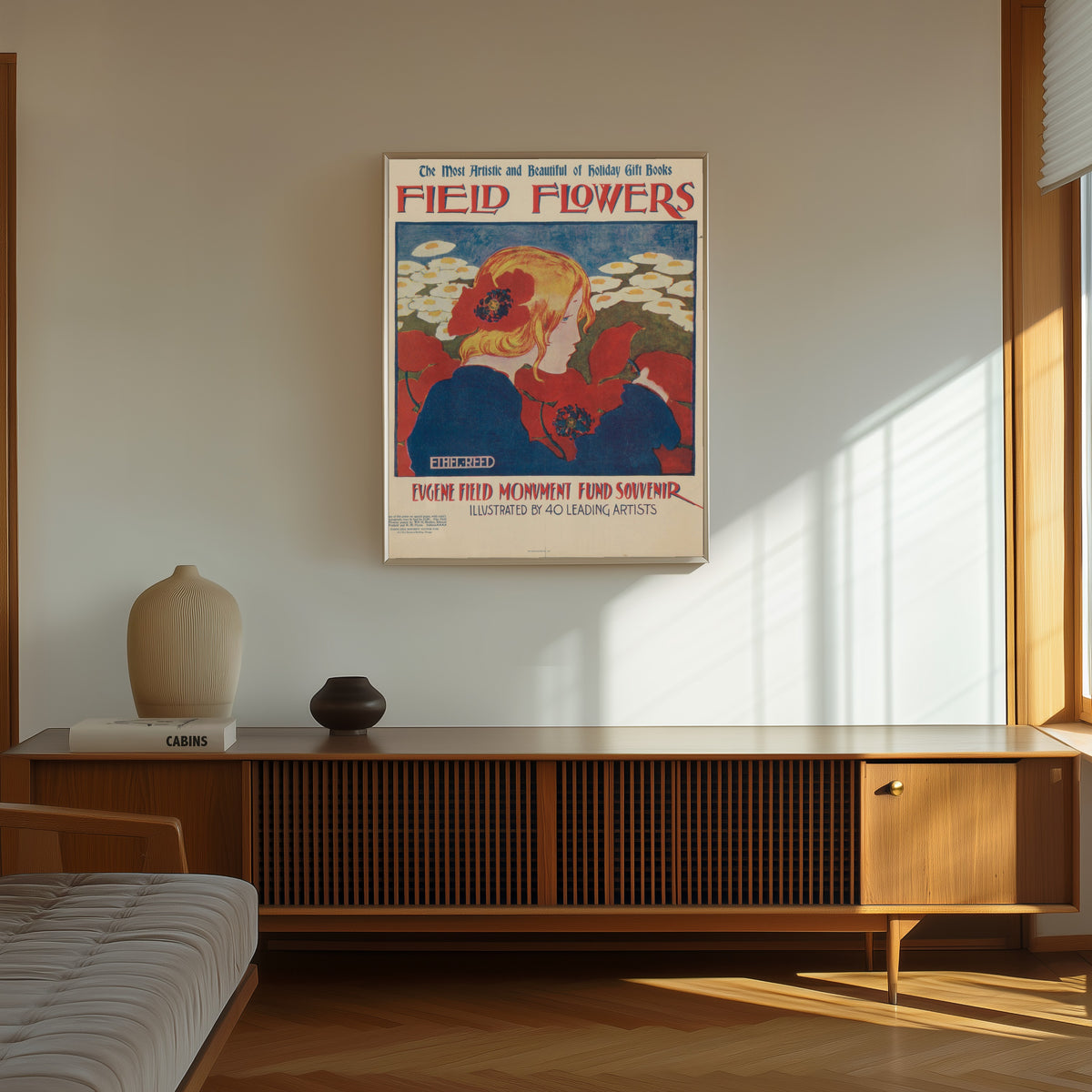 Framed art print of Field Flowers: The Most Artistic and Beautiful of Holiday… by Ethel Reed, in a thin light frame on a sunlit wall above a wooden sideboard