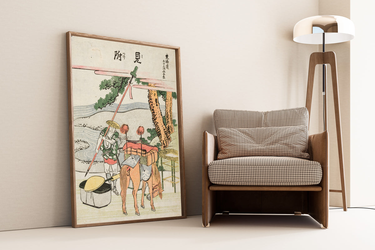 Framed art print of Fifty-three Stations of the Tōkaidō: Mitsuke by Katsushika Hokusai, leaning against a wall beside an armchair and a floor lamp