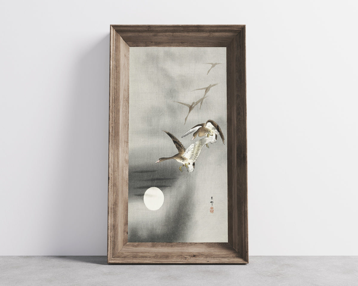 Framed art print of Five Geese in Flight at Full Moon by Ohara Koson, in a wide wooden frame leaning against a concrete wall
