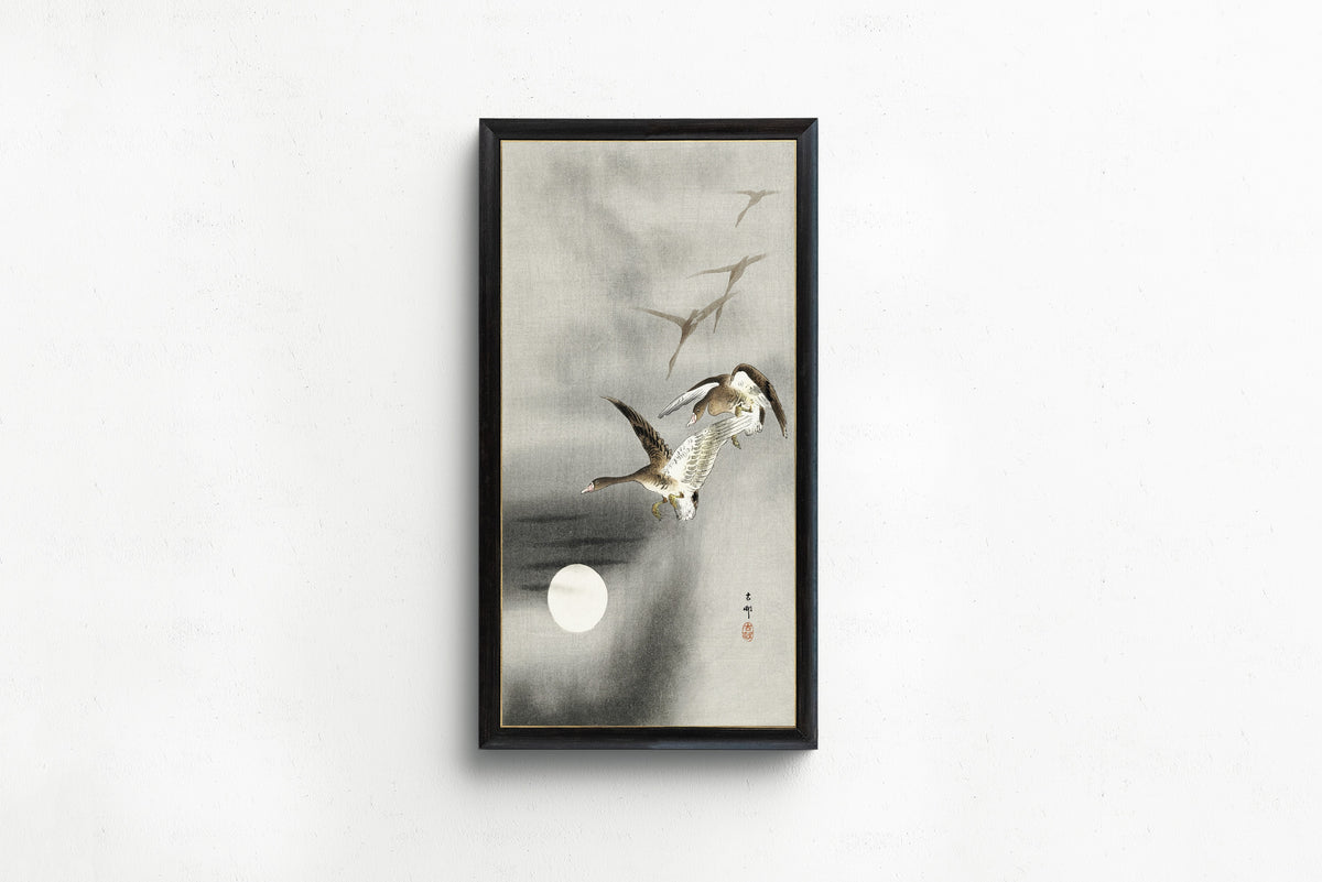 Framed art print of Five Geese in Flight at Full Moon by Ohara Koson, in a slim black frame on a plain white wall